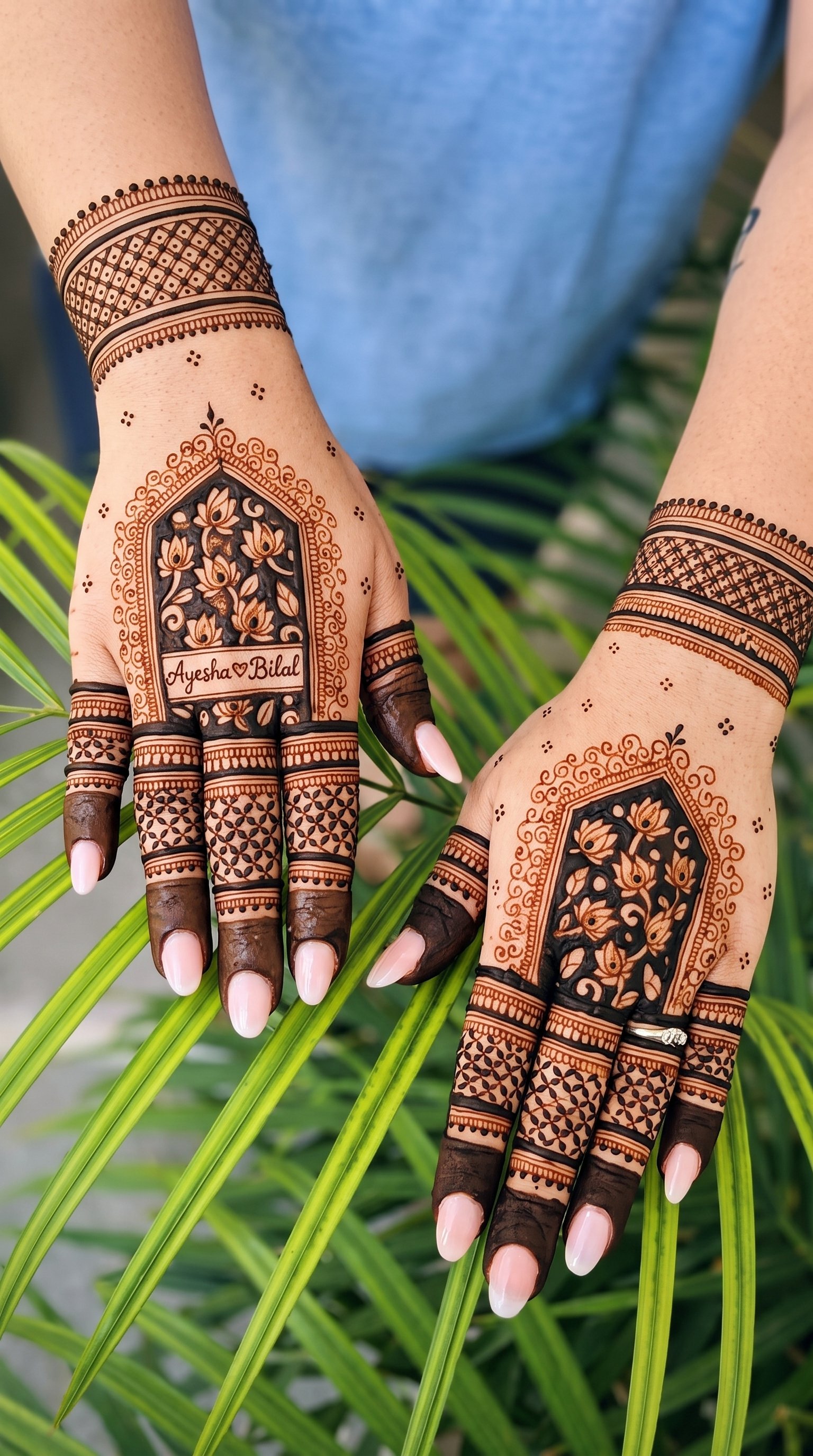 Pakistani bridal mehndi design featuring floral motifs, geometric patterns, and the names Ayesha and Bilal on the hands.