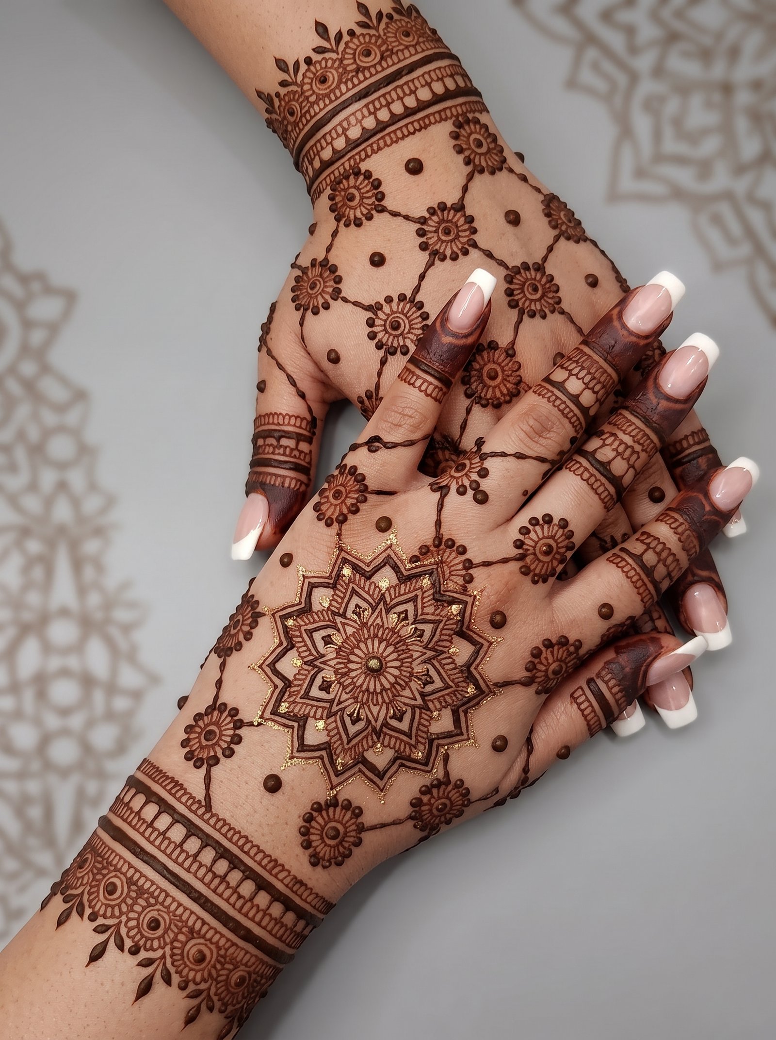 Decent mehndi design featuring a central floral mandala, small flower motifs, dotted patterns, and detailed wrist and finger bands.