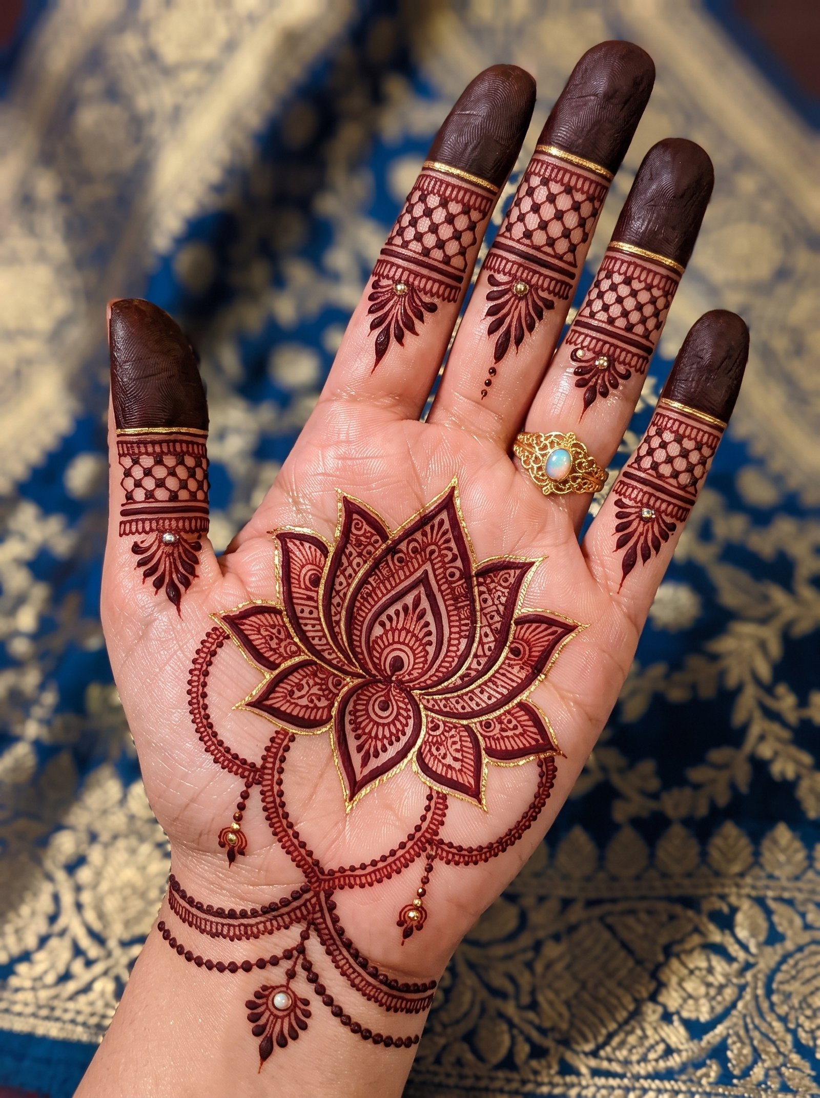 Front hand mehndi design featuring a large intricate lotus flower, decorative hanging chains, detailed finger patterns, and wrist bands.